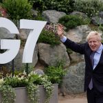 Boris Johnson waves in front of a G7 sign