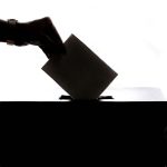 Black and white image of a hand putting an envelope in a voting box