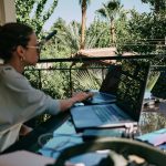 A woman working from a laptop on what looks to be a tropical balcony.